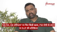 Man in a green polo being interviewed; white wall, plant on left, red Hindi news ticker across the bottom, The Journalist News logo top-right.