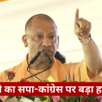 Man in orange robes speaks at a dais with two microphones, raising his index finger as he addresses the crowd; floral decor surrounds the podium, with a Hindi news banner at the bottom.