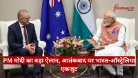 Two leaders seated in armchairs discussing in a formal meeting, with India and Australia flags behind them and a floral centerpiece between them.