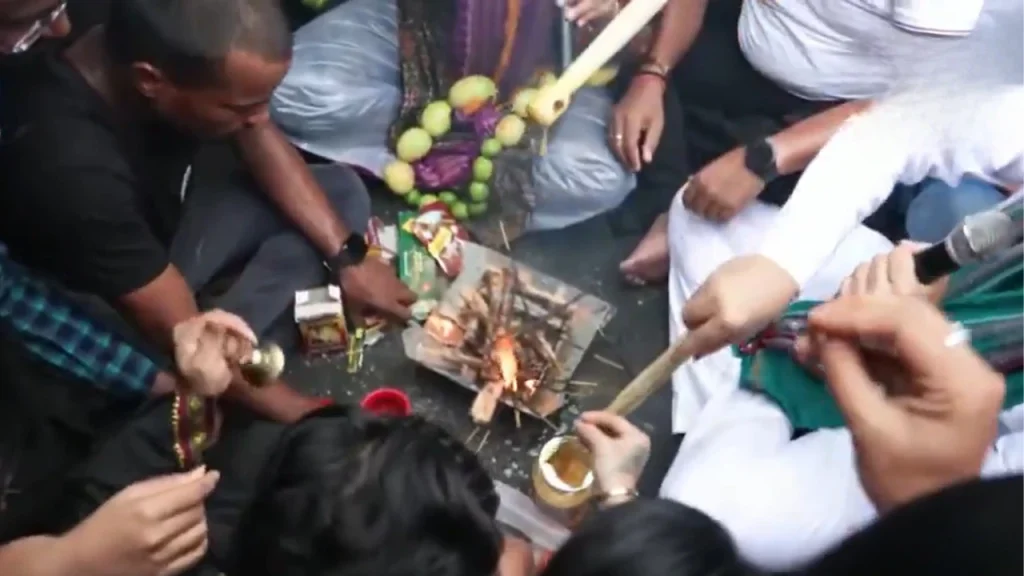 Light Blue and Yellow Bold Month Astrology Horoscope YouTube Thumbnail 31 - The Journalist News People sit in a circle around a small fire, adding sticks and offering items as part of a shared ritual, with fruit and snack boxes nearby.