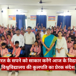 Group of students in pink shirts and brown uniforms posing in a classroom, many raising hands, with adults at the front and a red Hindi banner across the bottom.