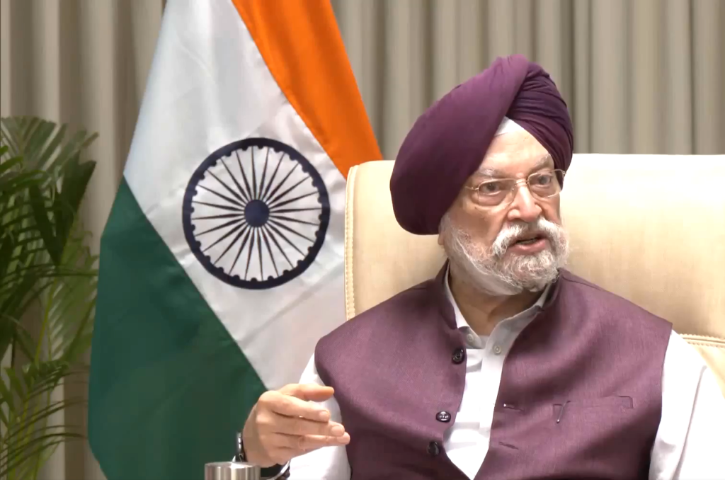 Senior man with a maroon turban and glasses speaks in a formal setting, Indian flag visible in the background.