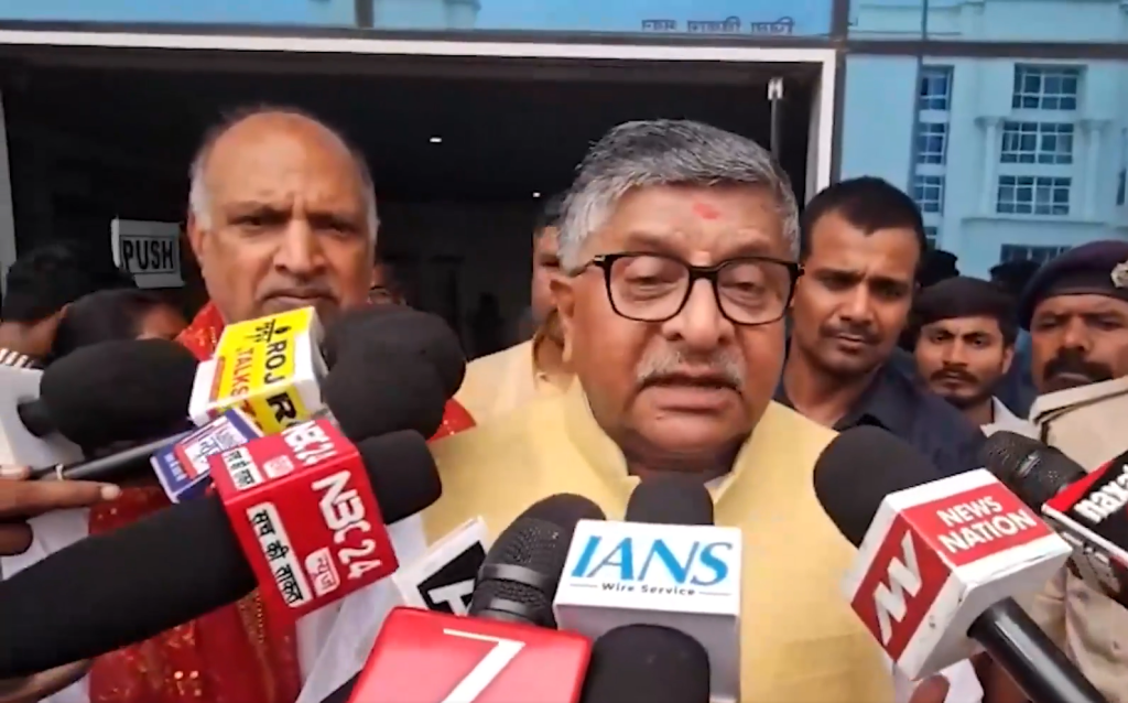 Screenshot 2026-07-09 154927 - The Journalist News Older man with glasses in a yellow kurta speaks to reporters, microphones held close outside a building.