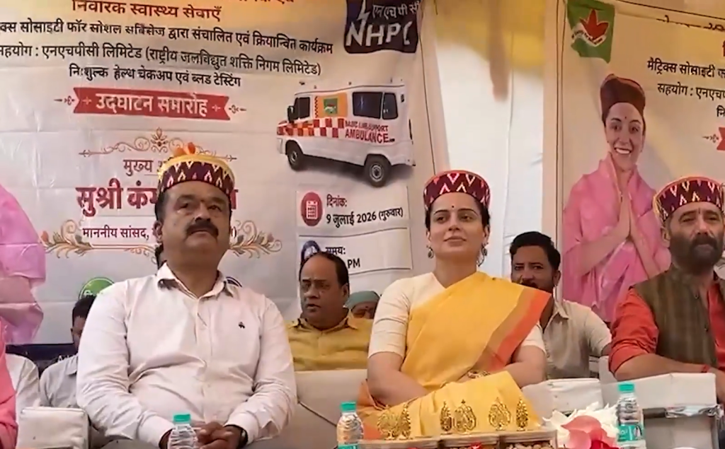 Screenshot 2026-07-09 210359 - The Journalist News Group of dignitaries seated on a stage at a health awareness event, with banners and a model ambulance in the background.