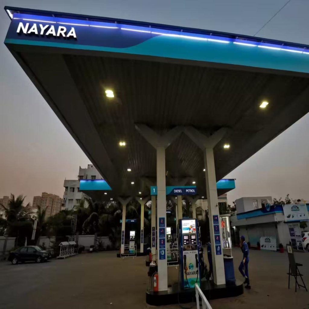 Nayara gas station canopy at dusk with multiple fuel pumps and blue signage reading Diesel and Petrol, a attendant nearby