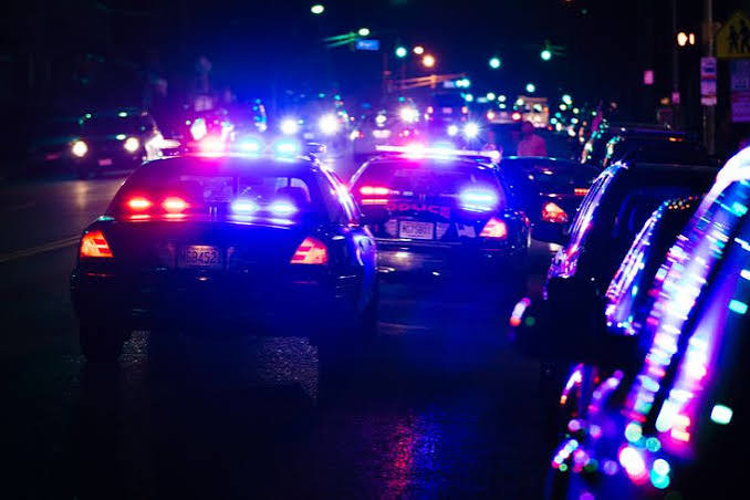 images 14 - The Journalist News Police cars with flashing red and blue lights on a nighttime city street, suggesting an active emergency or traffic stop.
