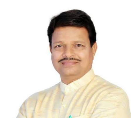 images 3 - The Journalist News Portrait of a man with a mustache wearing a pale-yellow kurta, facing the camera against a white background, smiling lightly on a plain backdrop.