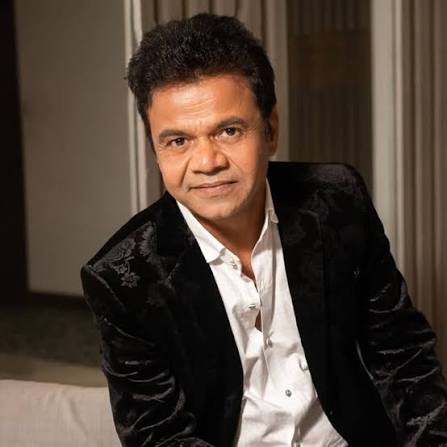 Man wearing a black velvet blazer and white shirt sits indoors, looking at the camera.