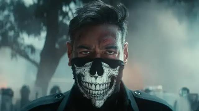 images 7 - The Journalist News Close-up of a man in a black jacket wearing a skull-pattern face mask, with smoke and trees in the background.