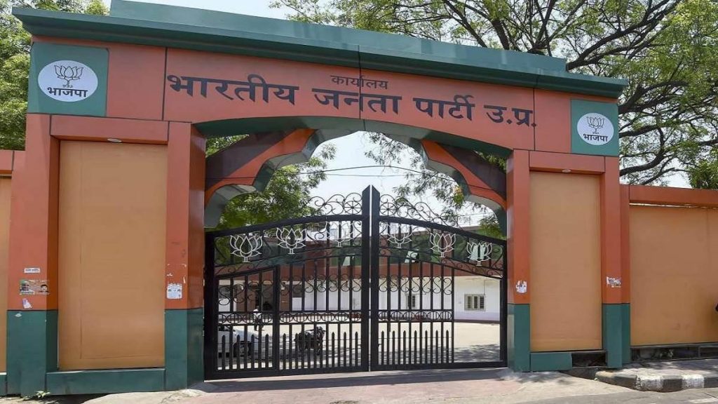 Entrance gate of a BJP building with orange walls and green trim, featuring the party logo on both sides and Hindi text above the archway